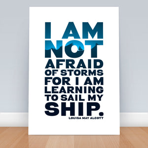 A4 print on floor against wall. Quote says "I am not afraid of storms for I am learning to sail my ship." The typography has a ship graphic in blue shades behind.